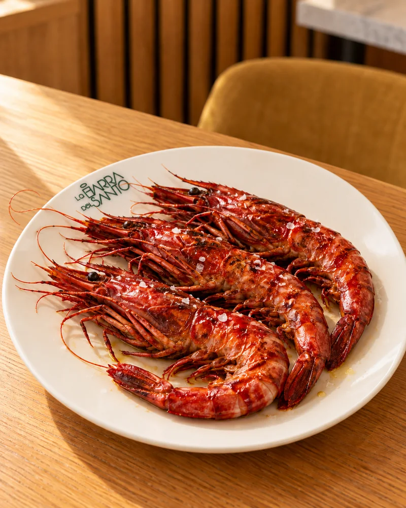 Carabineros sobre un plato blanco con el logotipo, en una mesa de madera.